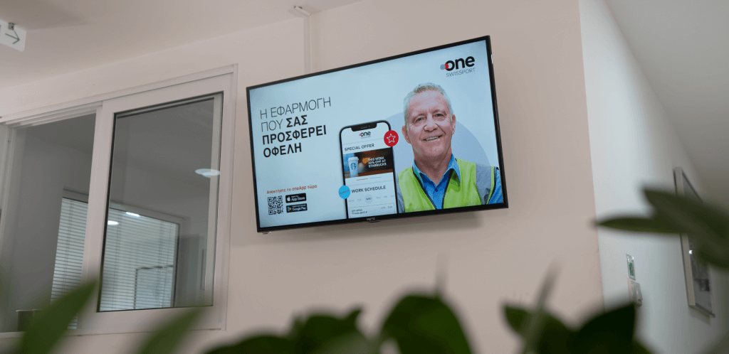 a digital signage screen showing a male Swissport employee smiling and the screen of a mobile phone