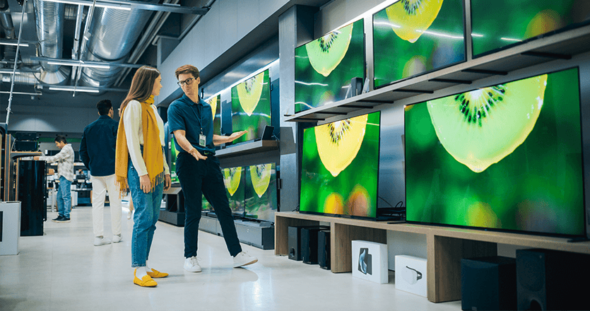 Two people in the TVs section of a technology store considering screens