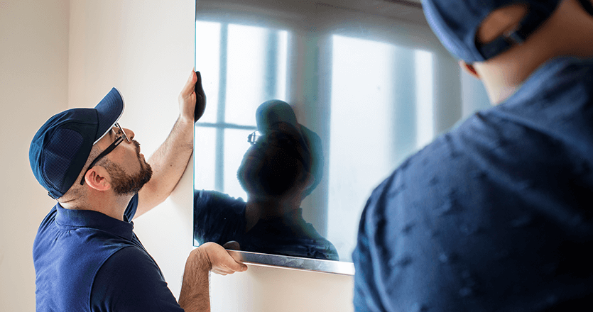 Two people are mounting a screen on a wall.