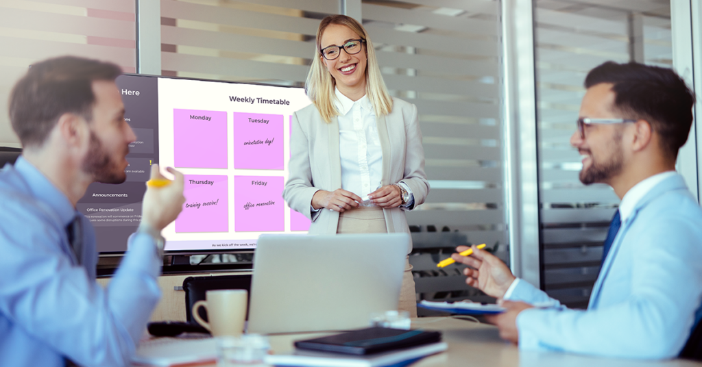 A meeting room with people discussing and a digital signage screen