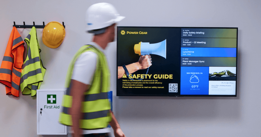 A worker in a safety vest walks past a digital screen displaying workplace safety guidelines.